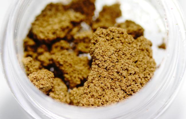 a translucent opened jar of bubble hash, a brown sand like substance