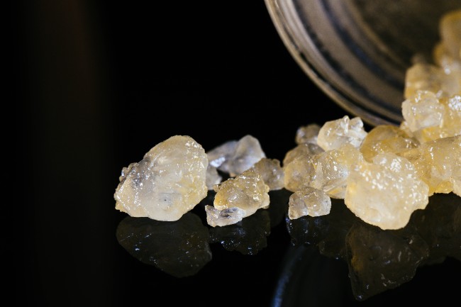 Yellowish, cream colored THCA diamonds shaped like perfect crystals are poured out on top of black surface