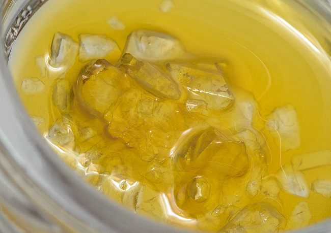 Yellow substance in a clear jar that has clear diamonds inside of it.