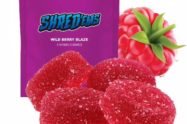 Red cannabis gummies covered in sugar crystals in front of a purple mylar bag with a raspberry beside it.