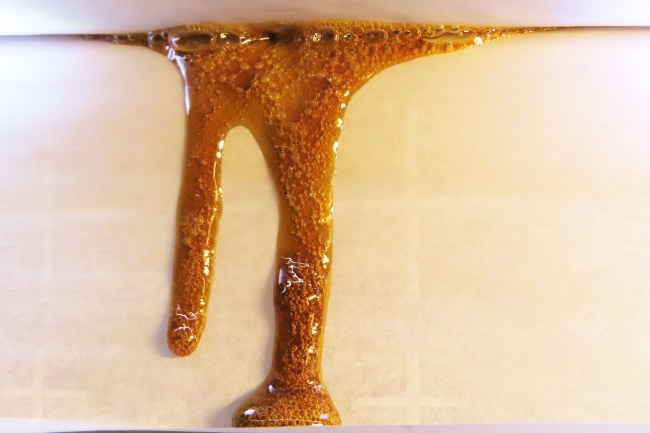 Brownish yellow concentrate liquid oozing from a crack in white parchment paper