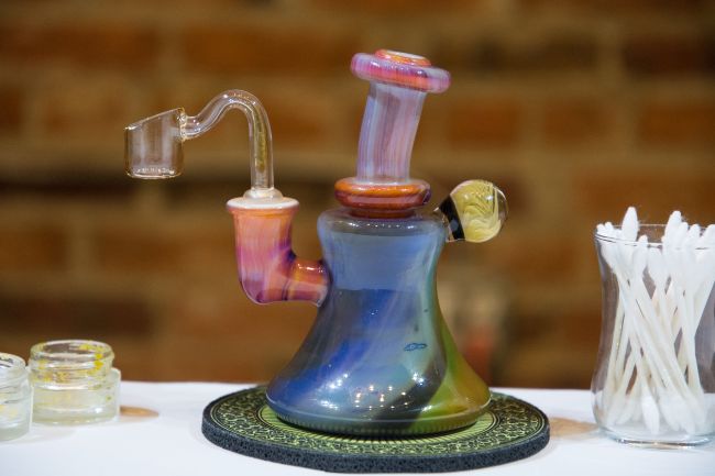 a multicolored dab rig with a pink mouthpiece and clear banger, against a brick wall